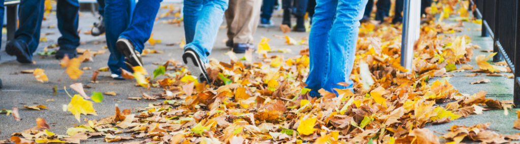 People walking through leaves on a sidewalk