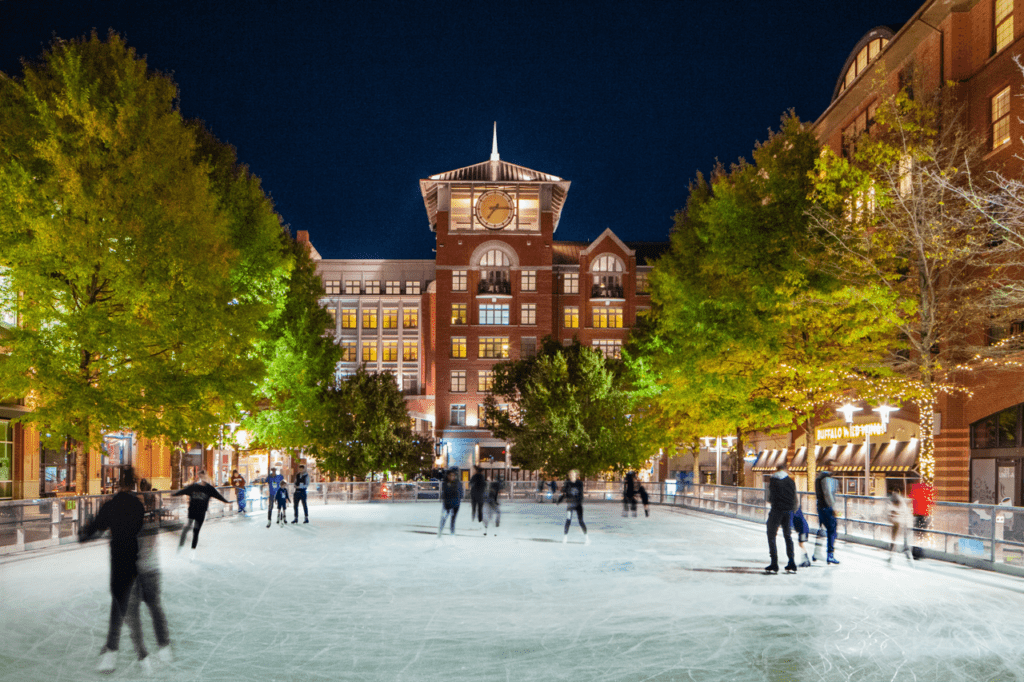 Rockville Town Square ice skating rink with ice skaters and the clocktower in the background.