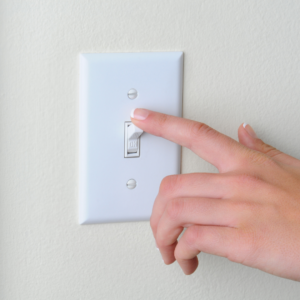Image depicts a person changing a light switch from the on position to off.