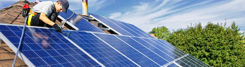 Image depicts a person on a residential roof installing solar panels.