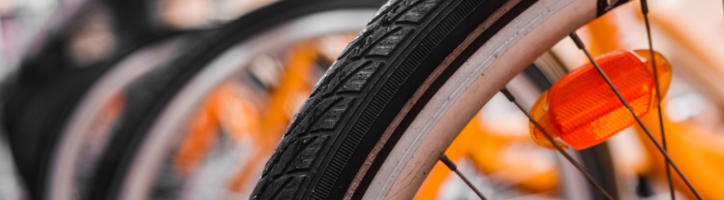 Image depicts a close up of a bicycle wheel in the foreground, with other bikes in the background.