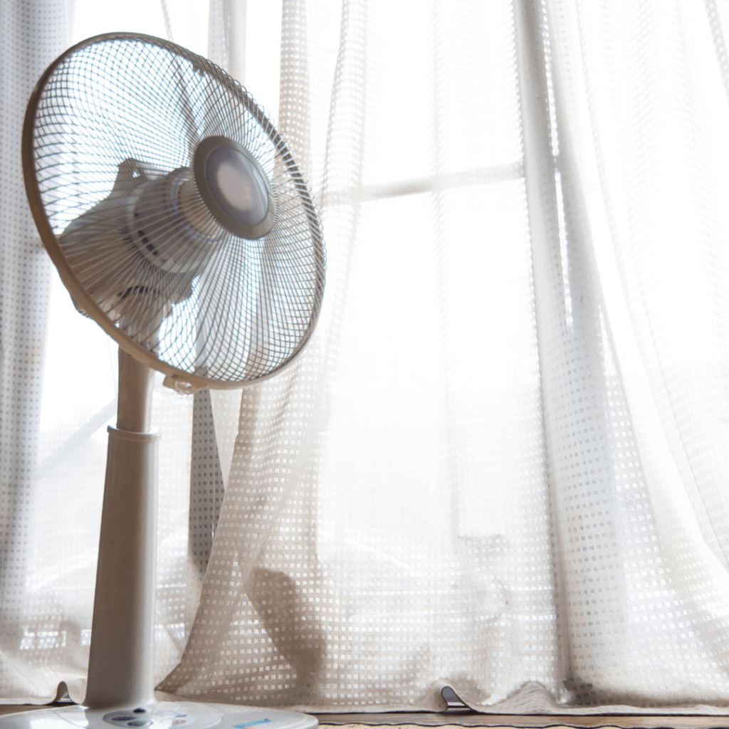 A fan blowing on the floor next to a window and drapes