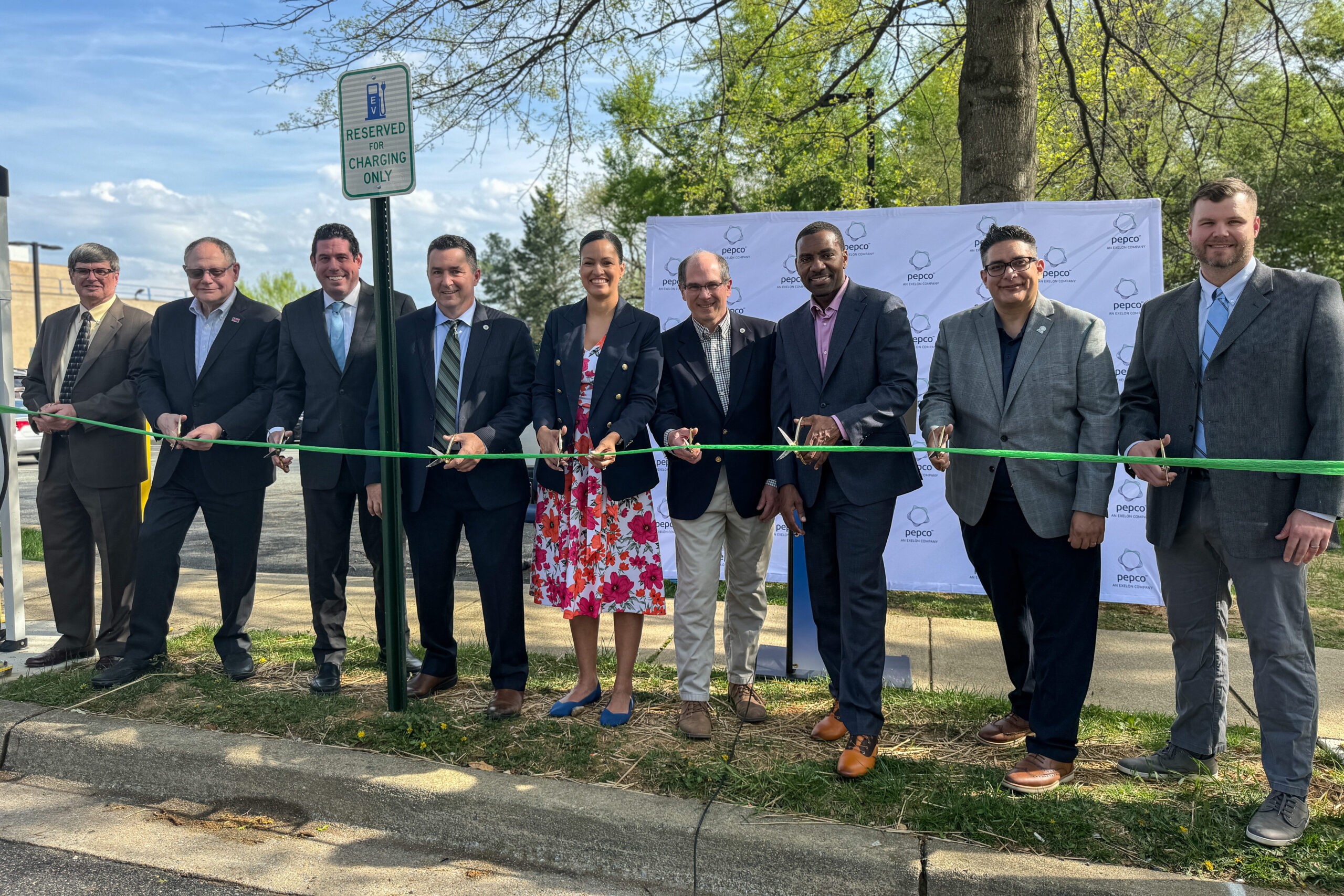 Members of the Montgomery County Council, Rockville Mayor and Council, the city’s Environment Commission, city staff and Pepco officials hold scissors and prepare to cut a green ribbon near a sign reading "Reserved for Charging Only" that is next to two new electric vehicle charging stations on Vinson Street.